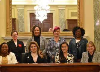 A group of women in front of a desk, posing for a picture while displaying a professional demeanor.